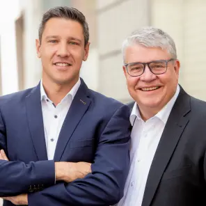 dunkelhaariger jüngerer Mann und grauhaariger Mann mit Brille