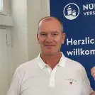 Mann mit weißem Polohemd vor Logo der NÜRNBERGER Versicherung