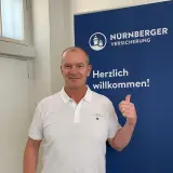 Mann mit weißem Polohemd vor Logo der NÜRNBERGER Versicherung