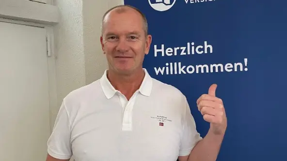 Mann mit weißem Polohemd vor Logo der NÜRNBERGER Versicherung