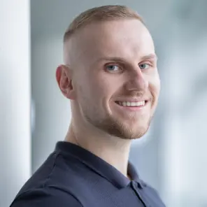 Mann mit blauem Poloshirt und kurzen blonden Haaren lächelt