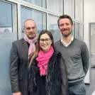 Mann mit rosa Schal und grauem Sakko, Frau mit pinkfarbenem Schal und dunkler Jacke, Mann mit Hemd und Pullover