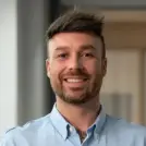Junger Mann mit hellblauem Hemd lächelt in die Kamera