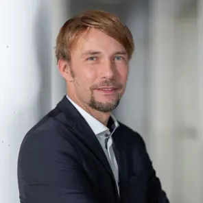 Mann mit Anzug steht mit verschränkten Armen an einer weißen Säule