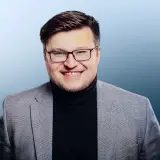 Junger Mann mit Brille in grauem Anzug und dunklen Pullover