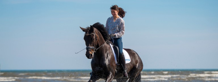 Frau auf Pferd die am Strand reitet 