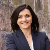 Frau mit kurzen braunen Haaren und Blazer lächelt