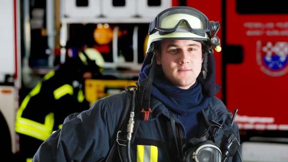 Junger Mann in Feuerwehrkleidung steht vor einem Feuerwehrauto