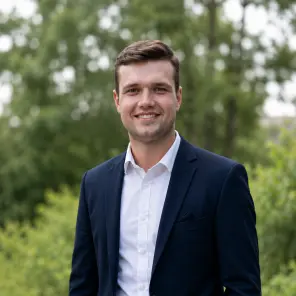 Mann im Anzug posiert vor einem Busch und lächelt