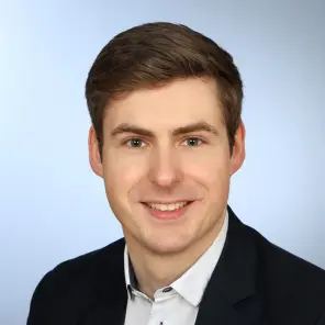 freundlich guckender junger Mann in weißem Hemd und schwarzem Jacket