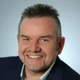 Mann mit kurzen Haaren und dünnem Bart lächelt