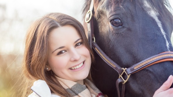 Junge Frau mit braunen Haaren streichelt ein dunkelbraunes Pferd