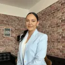 Frau mit schwarzen Haaren, die zu einem Zopf gebunden sind und hellblauem Blazer sitzt auf einem Stuhl