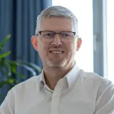 grauhaariger Mann mit Brille und weißem Hemd