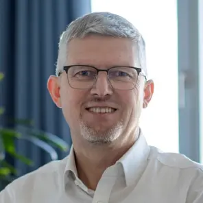 grauhaariger Mann mit Brille und weißem Hemd