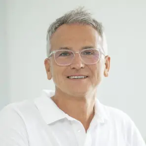 Grauhaariger Mann mit weißer Brille und weißem Poloshirt