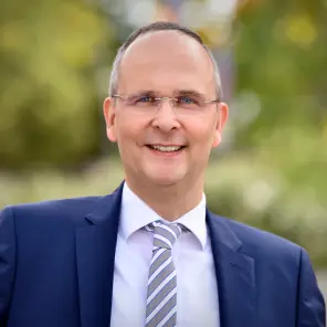 Mann mit Brille, blauem Sakko und blau-weiß gestreifter Krawatte