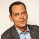 schlanker Mann mit hellblauem Hemd und grauem Sakko