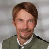 Mann mit kurzen braunen Haaren und grüner Stoffweste