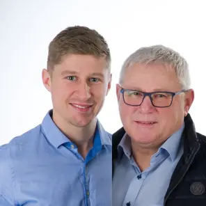 Ein junger und ein älterer Mann lächeln nebeneinander