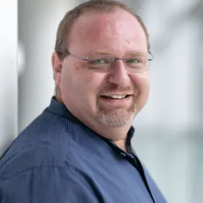 Mann mit Brille und blauem Hemd lächelt