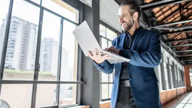 Ein Mann mit Laptop steht vor einer großen Fensterfront