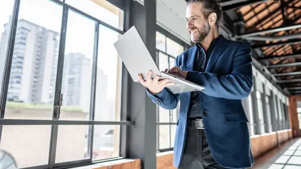 Ein Mann mit Laptop steht vor einer großen Fensterfront