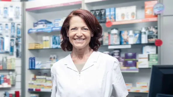 Frau mittleren Alters steht vor einem Regal in einer Apotheke