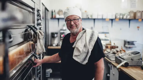 Mann mit weißer Mütze auf dem Kopf steht vor einem großen Backofen