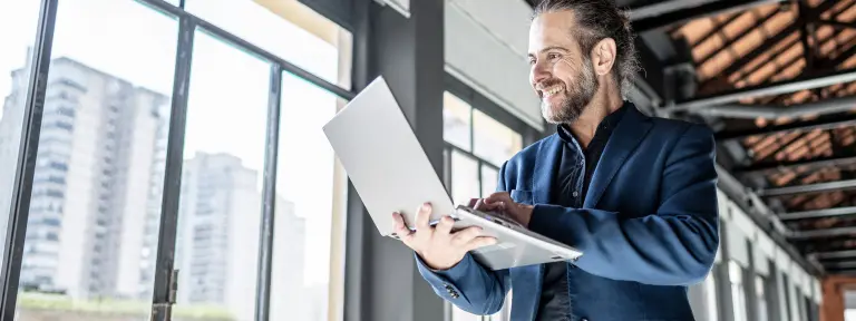 Ein Mann mit Laptop steht vor einer großen Fensterfront