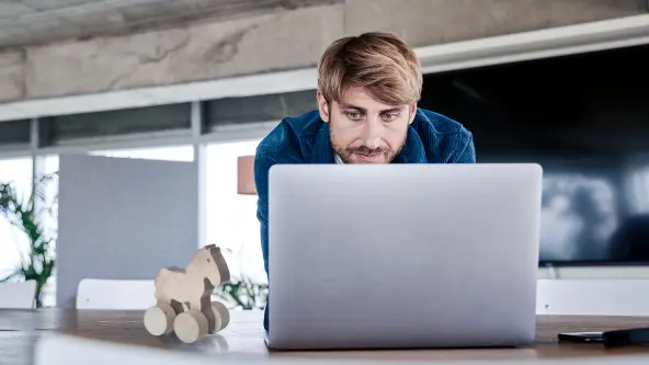 Junger Mann mit Bart schaut in seinen Laptop