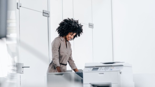 Frau mit vollen lockigen Haaren steht an einem großen Bürodrucker