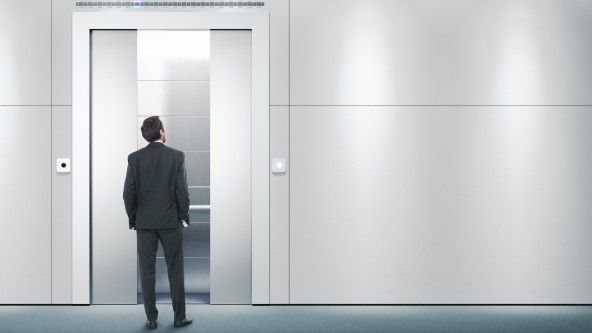 Mann in Anzug steht vor einer großen hellen Wand und wartet auf einen Aufzug