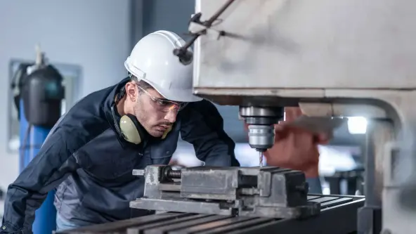 Mann mit weißem Helm und Schutzbrille bohrt mit einer großen Maschine etwas