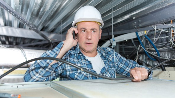 Mann mit Bauhelm auf dem Kopf telefoniert auf einer Baustelle