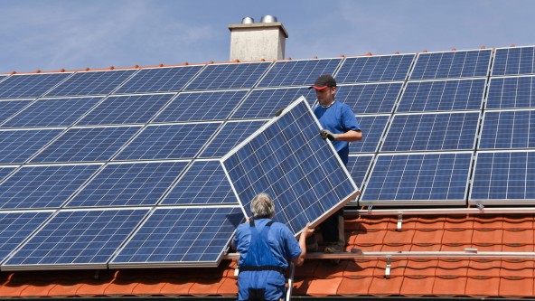 2 Männer in blauer Kleidung montieren Solarmodule auf einem Hausdach