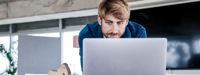 Junger Mann mit Bart schaut in seinen Laptop
