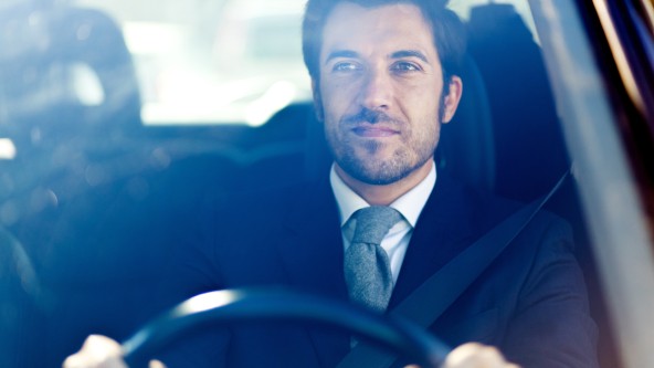 Mann in Hemd und mit Krawatte sitzt am Steuer eines Autos