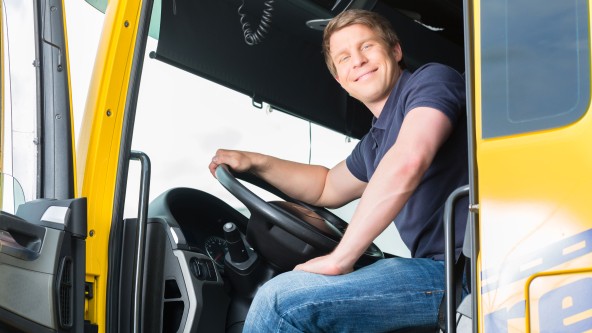 Mann im T-Shirt sitzt in einem LKW und lacht aus der geöffneten Fahrertür