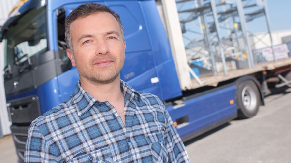 Mann in kariertem Hemd steht vor einem blauen Lastwagen
