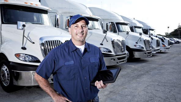 Mann in blauem Hemd und blauer Cape steht vor mehren grauen Lastwagen