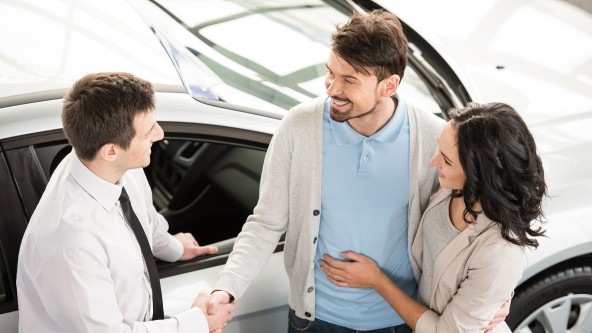 Junges Paar spricht mit einem Mann mit Krawatte vor einem neuen Auto
