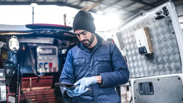 Handwerker steht vor einem offenen Transporter mit Handschuhen und tippt auf ein Tablet