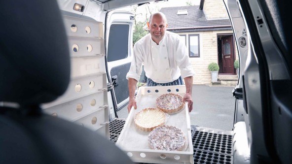 Mann mit weißem Hemd hebt eine Box mit 3 Kuchen in einen Transporter