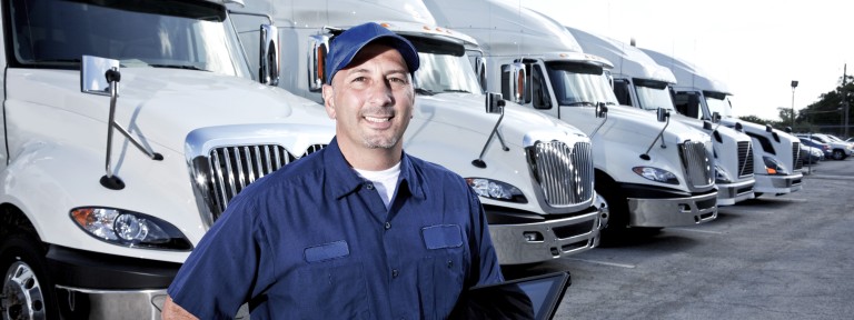 Mann in blauem Hemd und blauer Cape steht vor mehren grauen Lastwagen