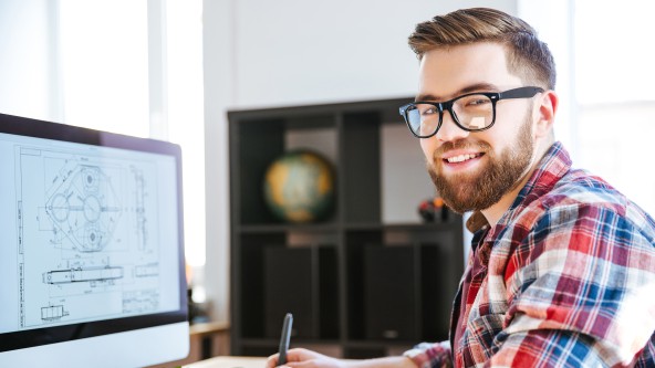Mann mit Brille und Vollbart sitzt vor Plänen auf einem Monitor