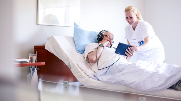 Pflegerin zeigt Mann in einem Bett etwas am Tablet