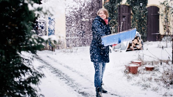 Frau befreit Gehweg von Schnee