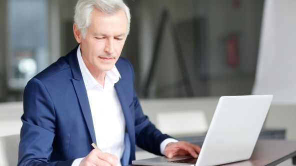 Älterer Mann in Anzug arbeitet konzentriert an einem Laptop