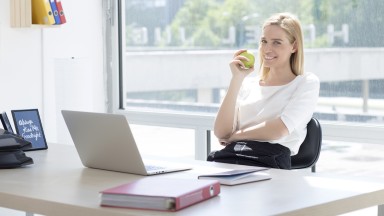 Junge Frau hat grünen Apfel in der Hand und sitzt vor einem aufgeklappten Laptop